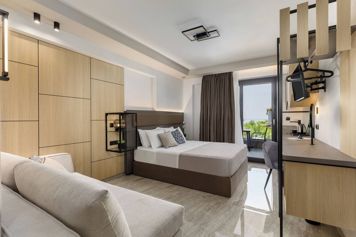A modern hotel room with a large bed, a desk, and a sofa.