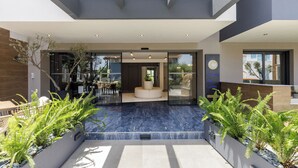 A modern building with a glass entrance, indoor seating area, and outdoor plants. - Costa De Luxe Suites (Dio-Olympos)