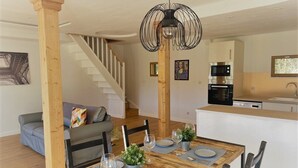 Ein Essbereich mit Holztisch, gedeckt für vier Personen, einer Treppe im Hintergrund und einer Küche mit modernen Geräten.