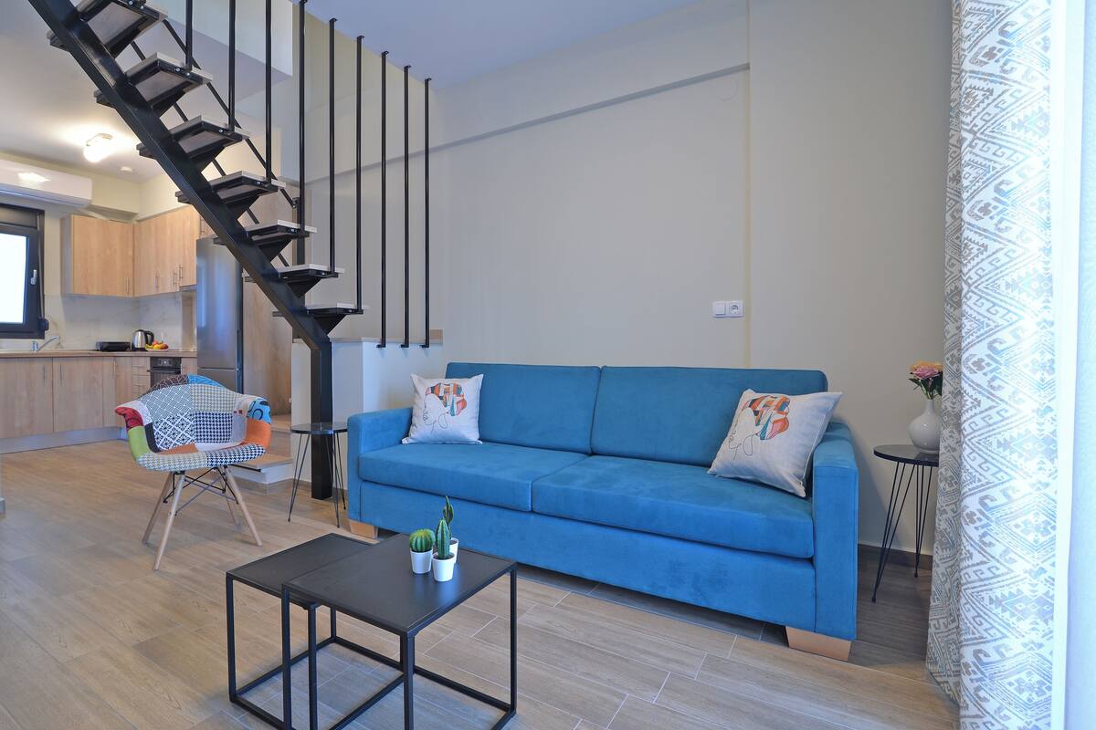 Una sala de estar moderna con un sofá azul, una mesa de centro negra y una escalera.