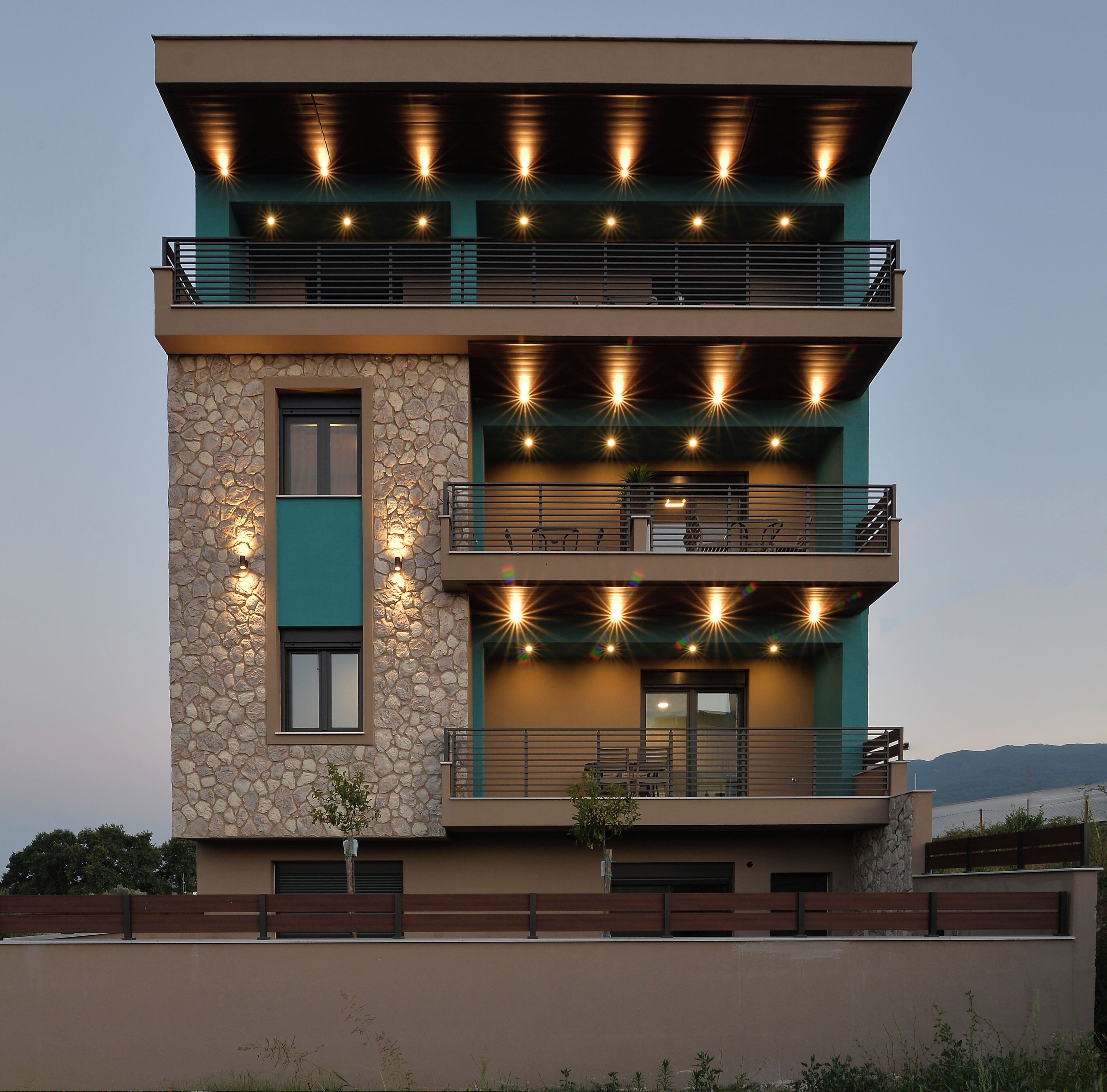 Un edificio moderno de varios pisos con balcones, fachada de piedra y zona de estar al aire libre.