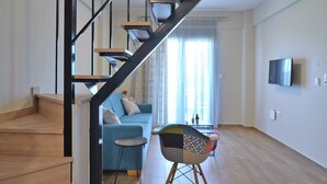 Ein modernes Wohnzimmer mit einer Holztreppe, einem blauen Sofa, einem kleinen runden Tisch und einem Fernseher an der Wand.