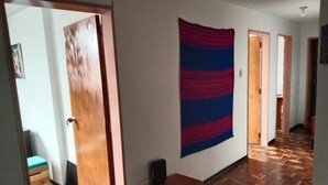 Un couloir doté d’un parquet en bois, d’une grande tapisserie abstraite accrochée au mur et d’un meuble en bois.
