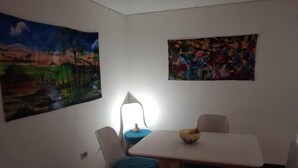 Un coin repas avec une table et des chaises, une lampe et deux tableaux accrochés aux murs.