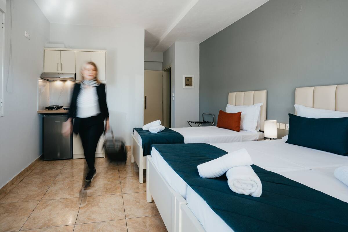 A hotel room with two beds, a kitchenette, and a bathroom.