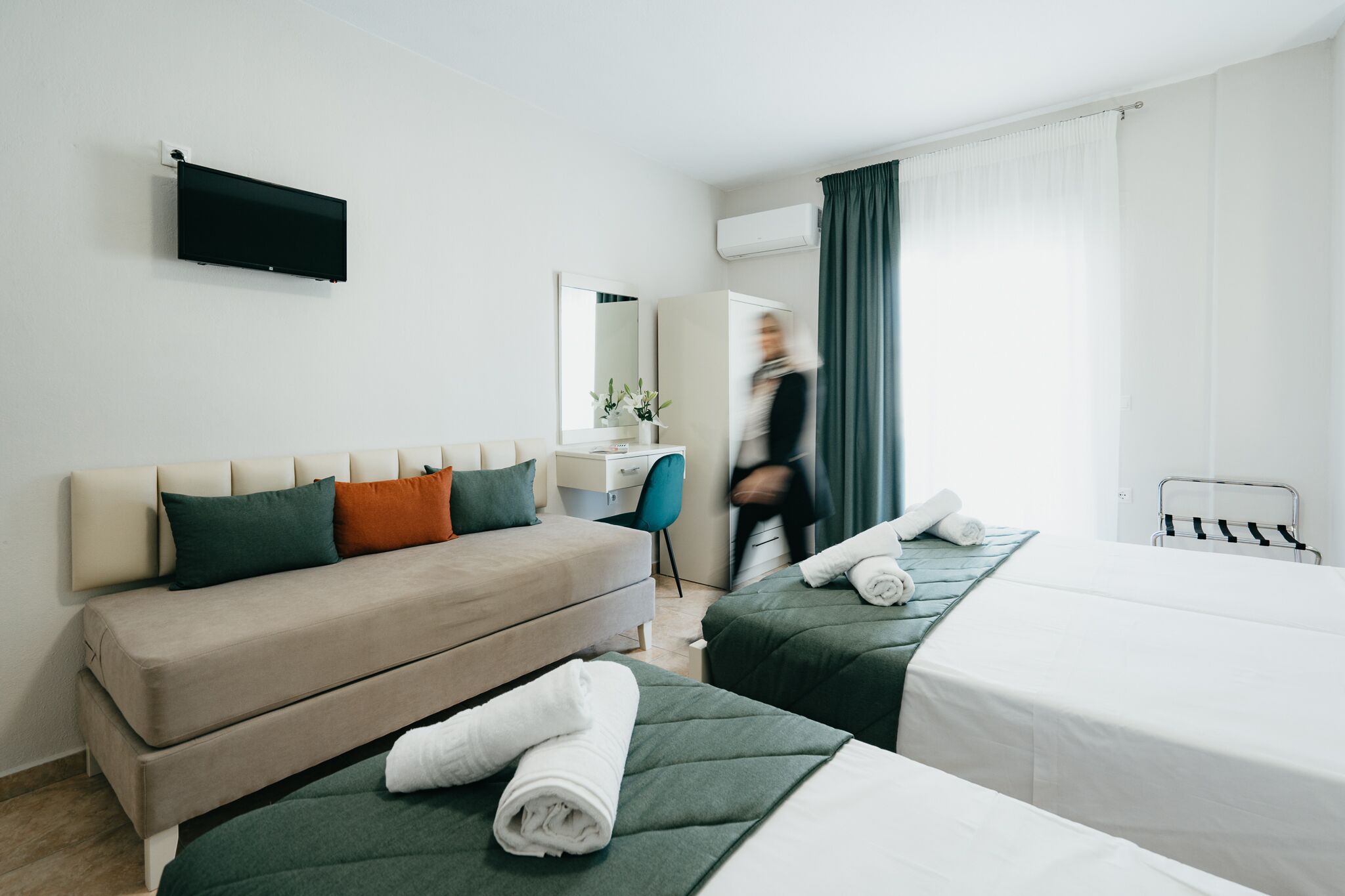 Et hotelværelse med sofa, to enkelt senge, et skrivebord og et fjernsyn ophængt på væggen.