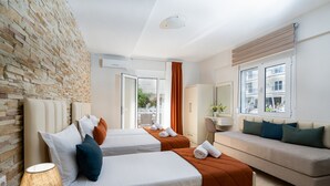 A hotel room with two beds, a sofa, a desk, and a stone wall. - Angela Rooms (Dio-Olympos)