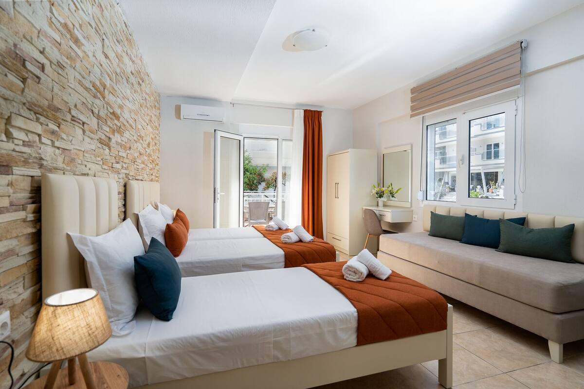 A hotel room with two beds, a sofa, a desk, and a stone wall.