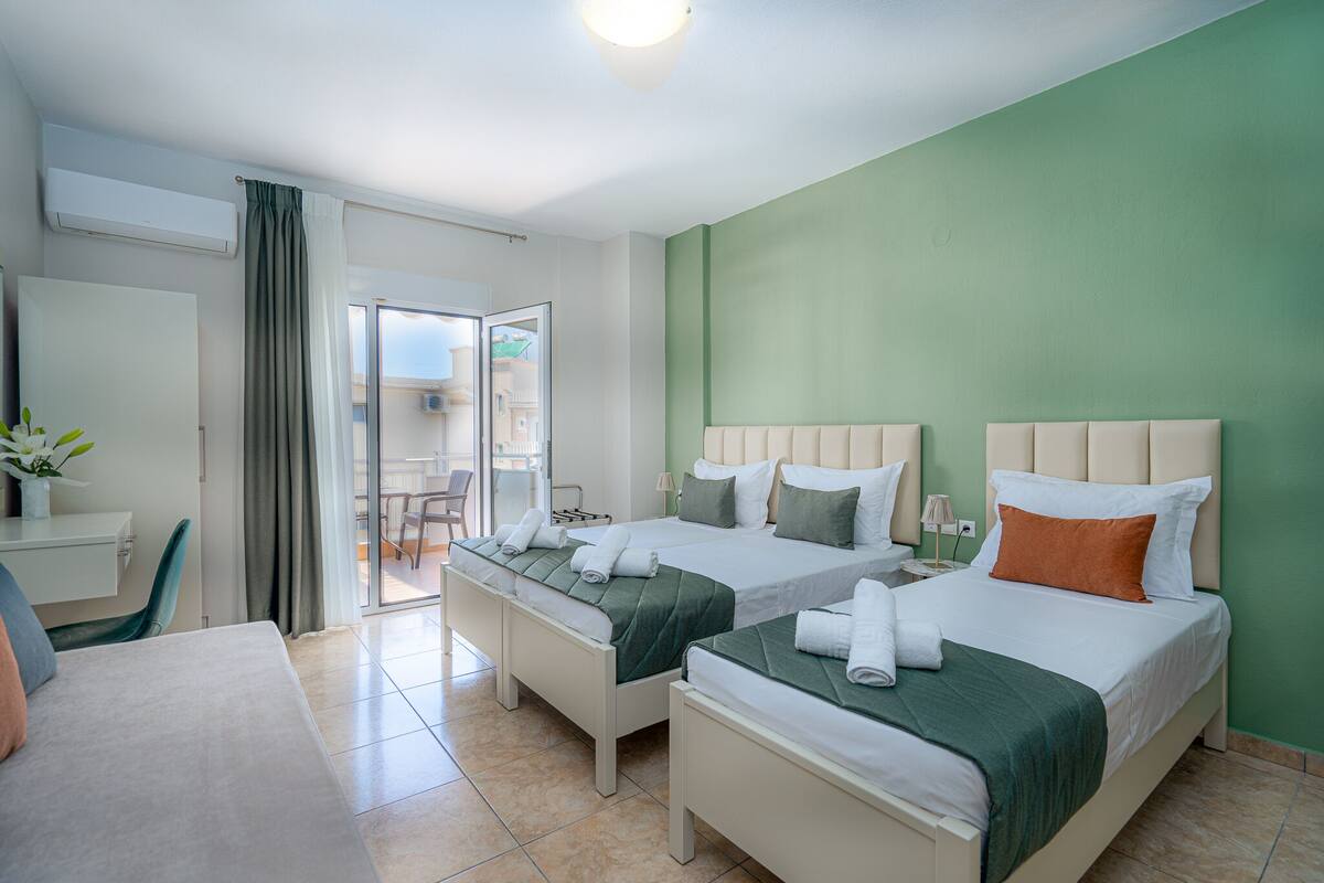 A hotel room with two beds, a desk, and a chair. There is a balcony with a view.