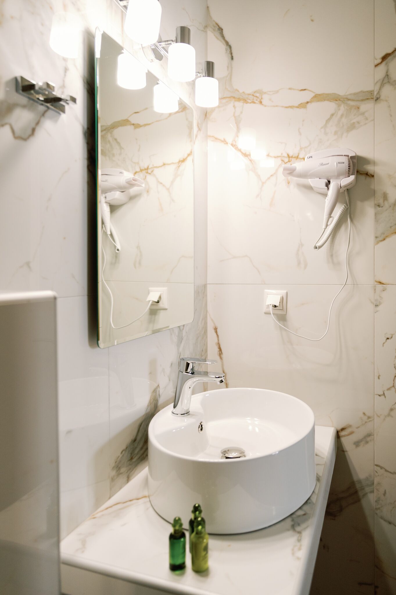 Ein Badezimmer mit einem runden Waschbecken, einem Spiegel und zwei an der Wand befestigten Haartrocknern.