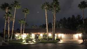 Ein Haus mit Ziegeldach, umgeben von Palmen und beleuchtet durch Außenbeleuchtung.