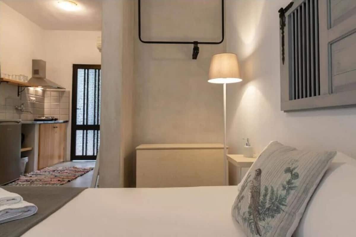 Ein Schlafzimmer mit Bett, Nachttisch, Lampe und Blick zur Küche.