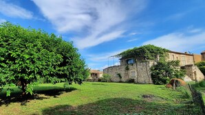Un bâtiment en pierre, surmonté d’un toit en pierre, entouré d’une pelouse et d’un grand arbre.