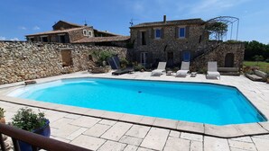 Une piscine avec des chaises longues, des murs en pierre et un bâtiment en pierre doté de nombreuses fenêtres.