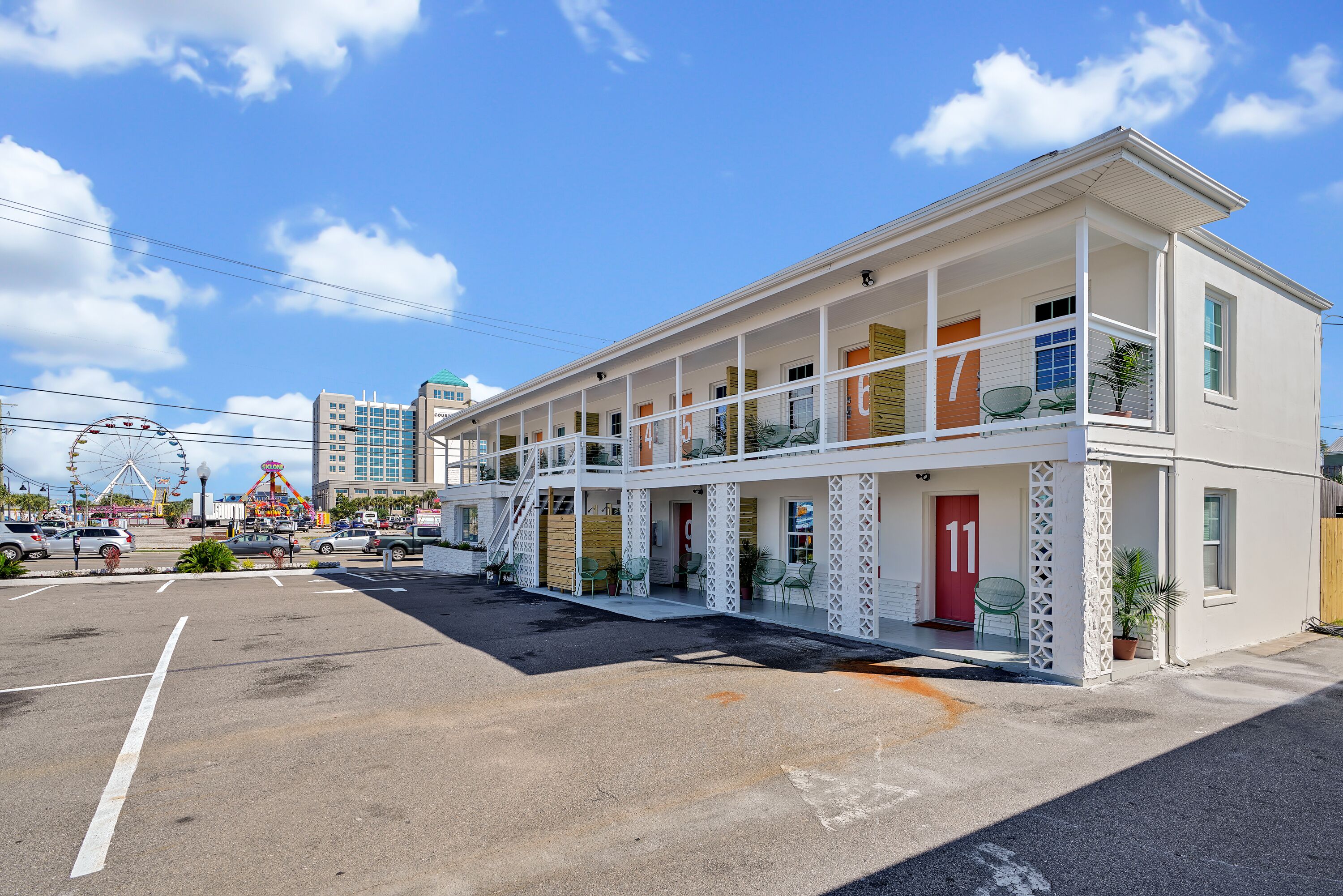A two-story motel with a balcony on the second floor, a parking lot in front, and a Ferris wheel in the background.