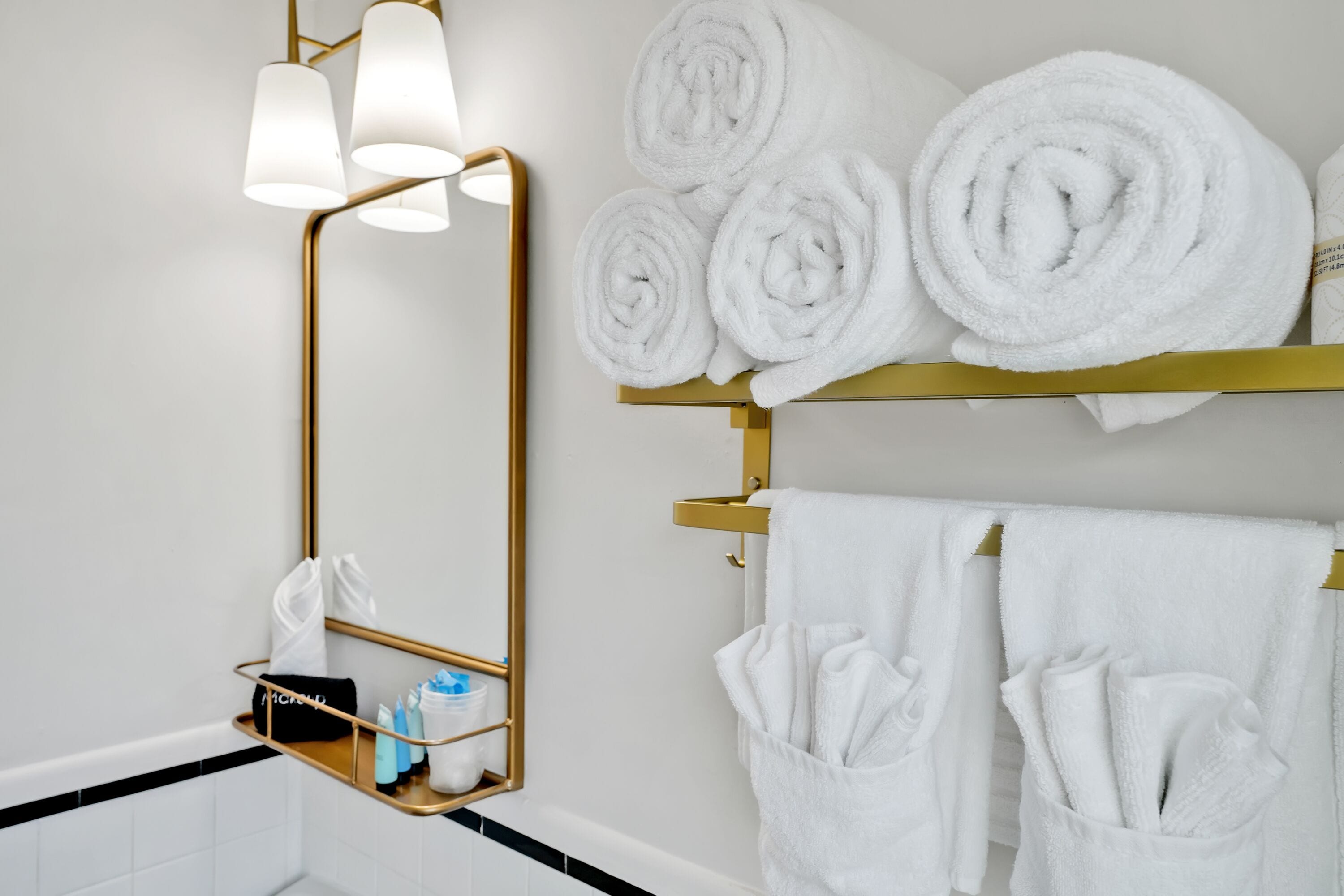 A bathroom with a gold-framed mirror, white towels, and a towel rack.