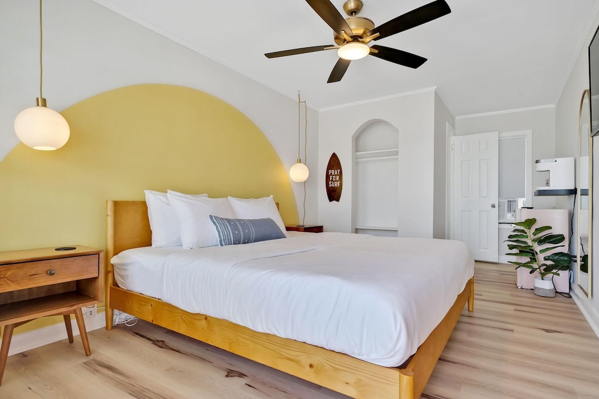 A bedroom with a wooden bed, bedside tables, a ceiling fan, and a wall-mounted surfboard.