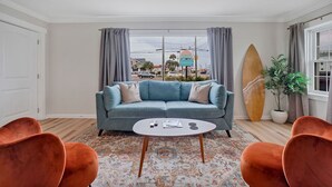 A living room with a blue sofa, orange chairs, a round coffee table, and a surfboard. - The Starlite Inn (Carolina Beach)