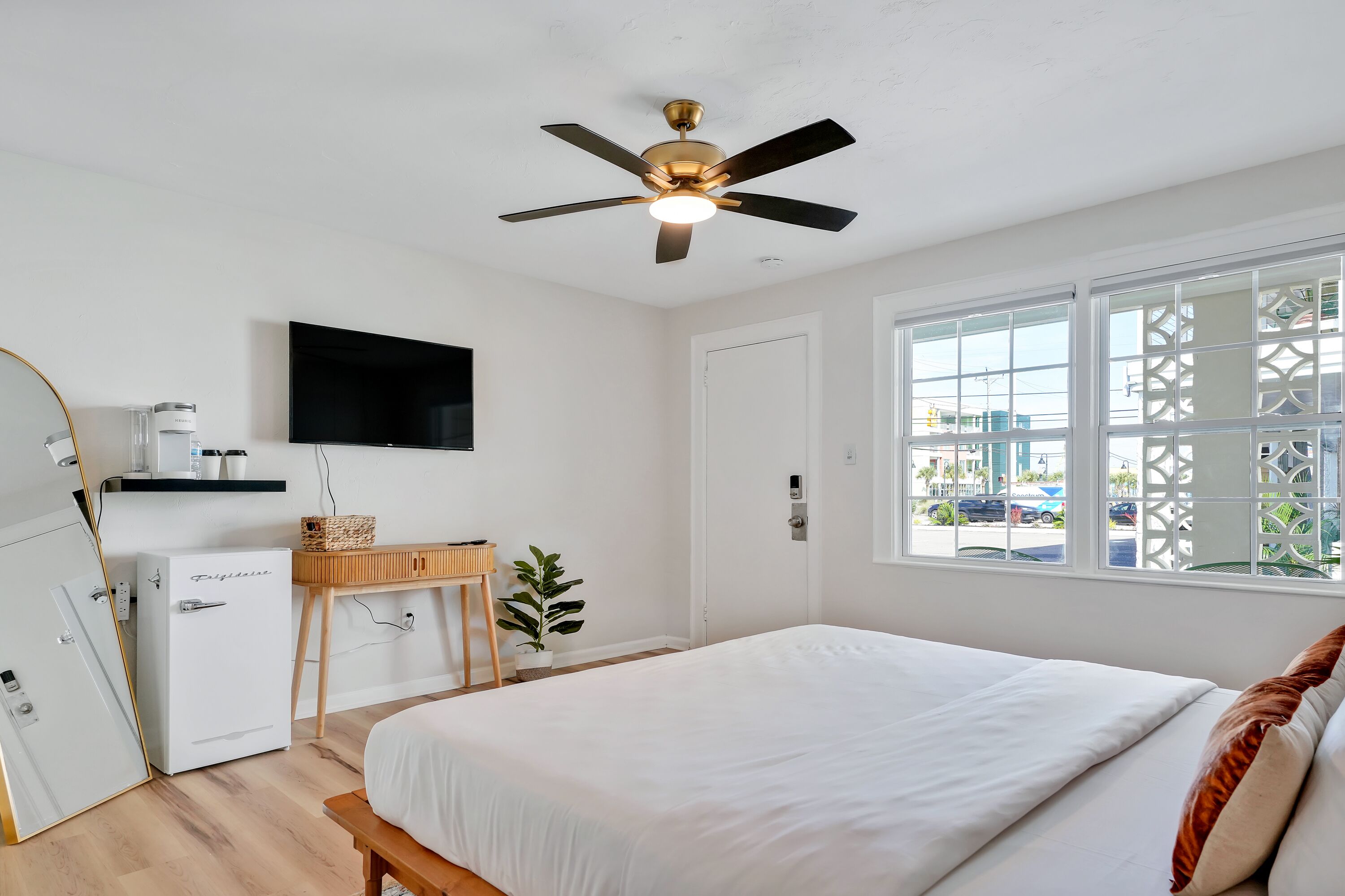 Habitación de hotel con cama, escritorio con televisor, máquina de café, refrigerador pequeño y ventana con vista al exterior.