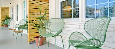 Una zona de estar al aire libre techada, con sillas de metal verde y plantas en macetas.