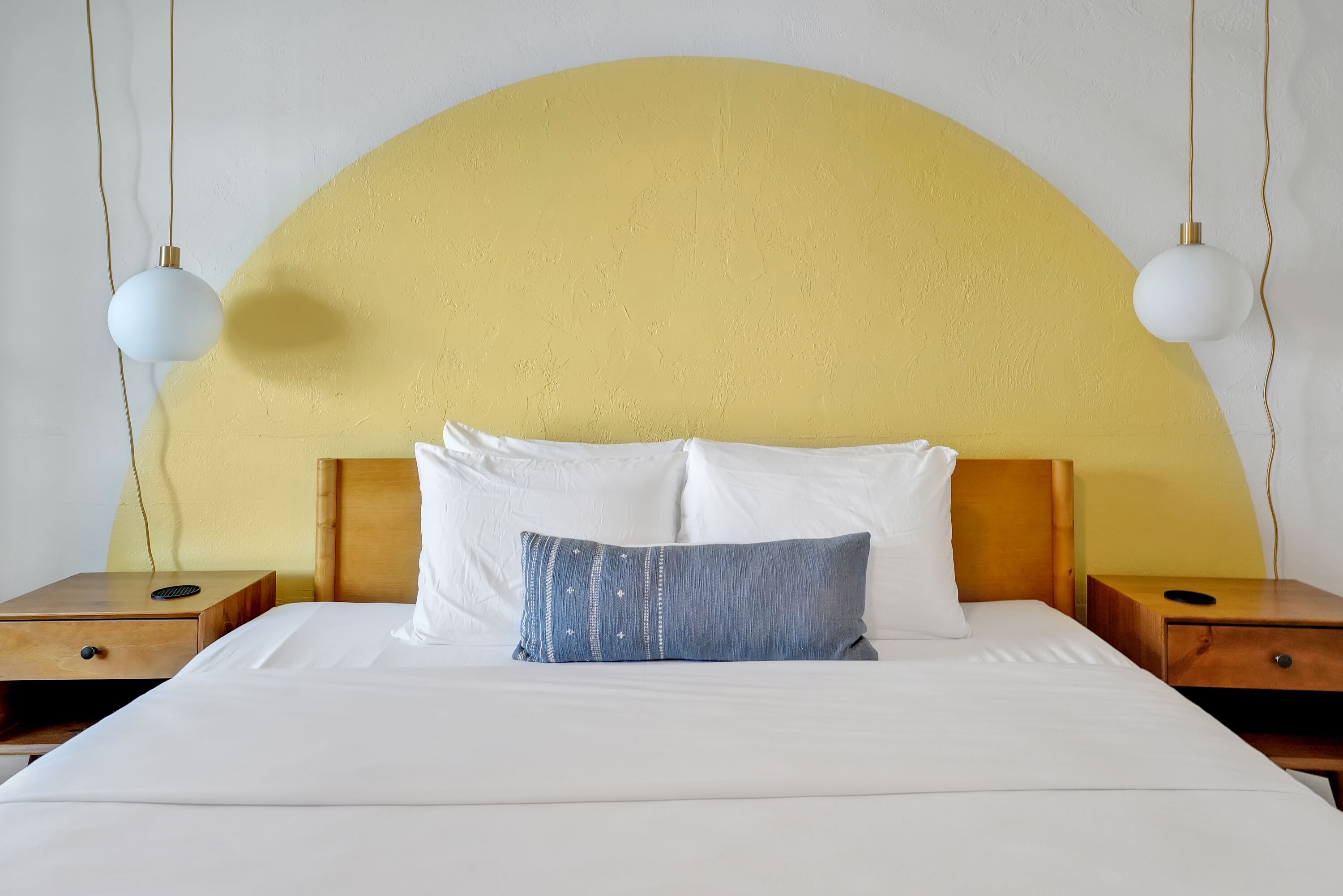 Una cama con ropa de cama blanca, una almohada azul y un cabecero de madera. Hay dos mesitas de noche con lámparas.