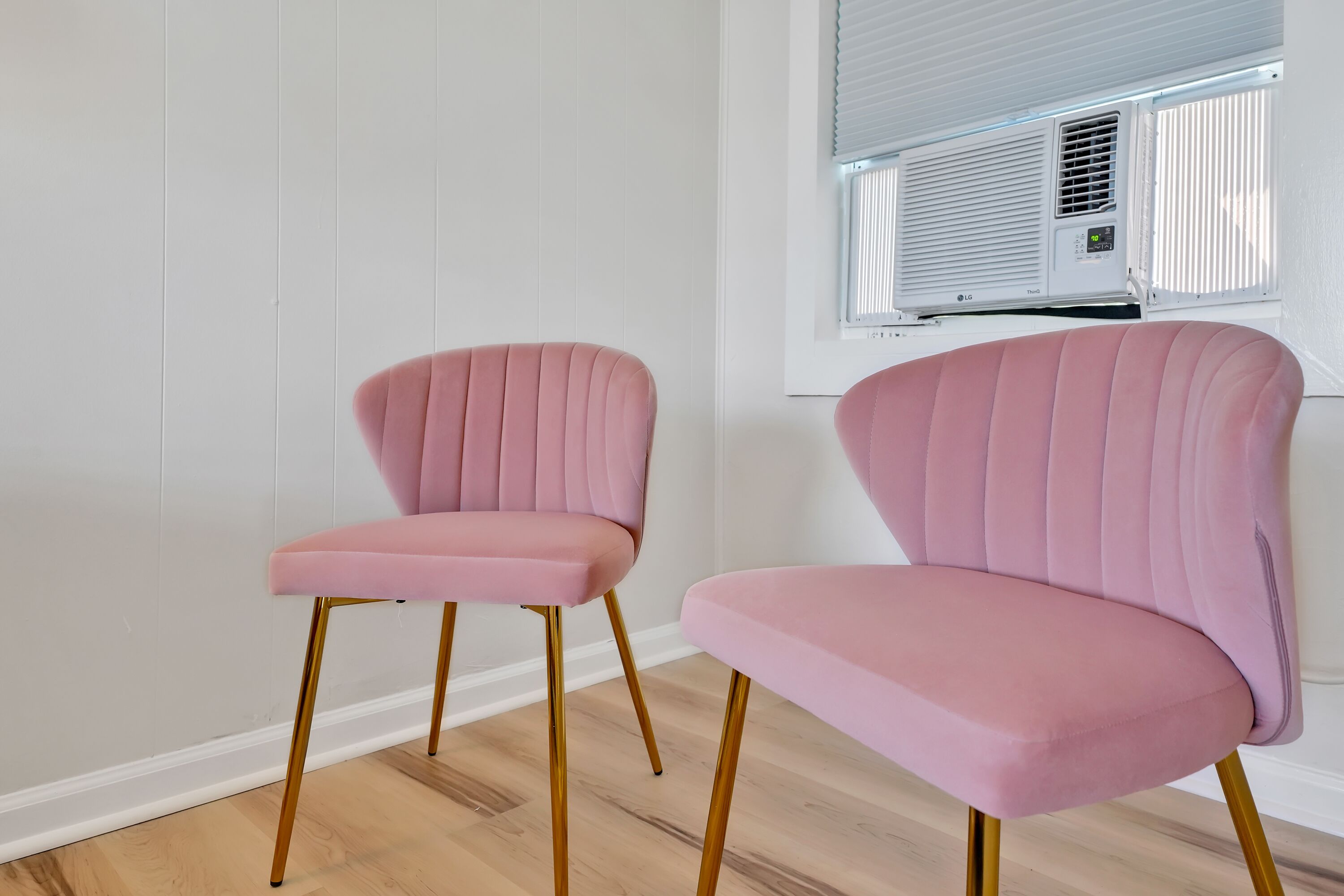 Twee roze fauteuils met gouden poten in een kamer met houten vloer en een witte muur.