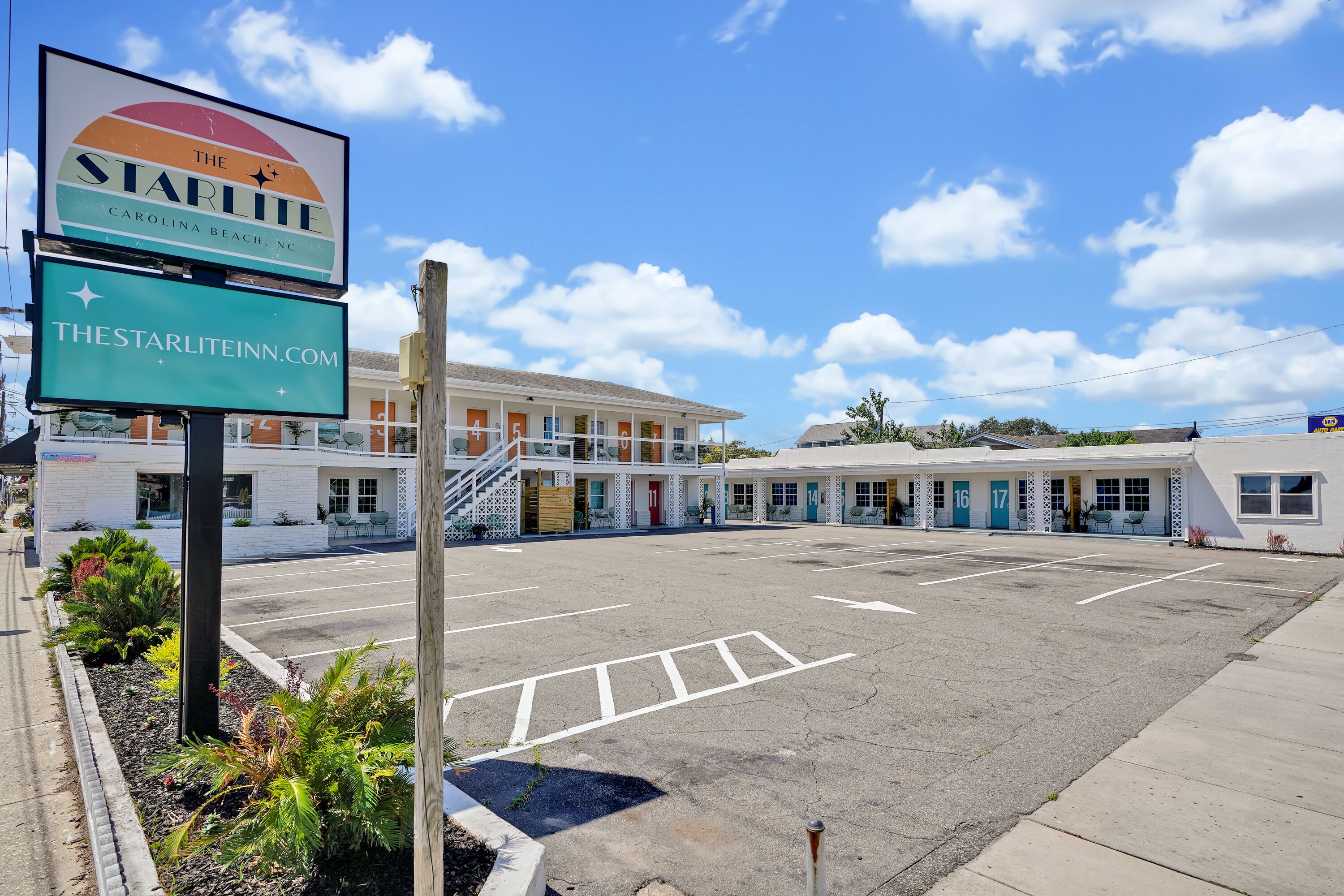 A motel with a parking lot, a signboard, and a building with multiple rooms.