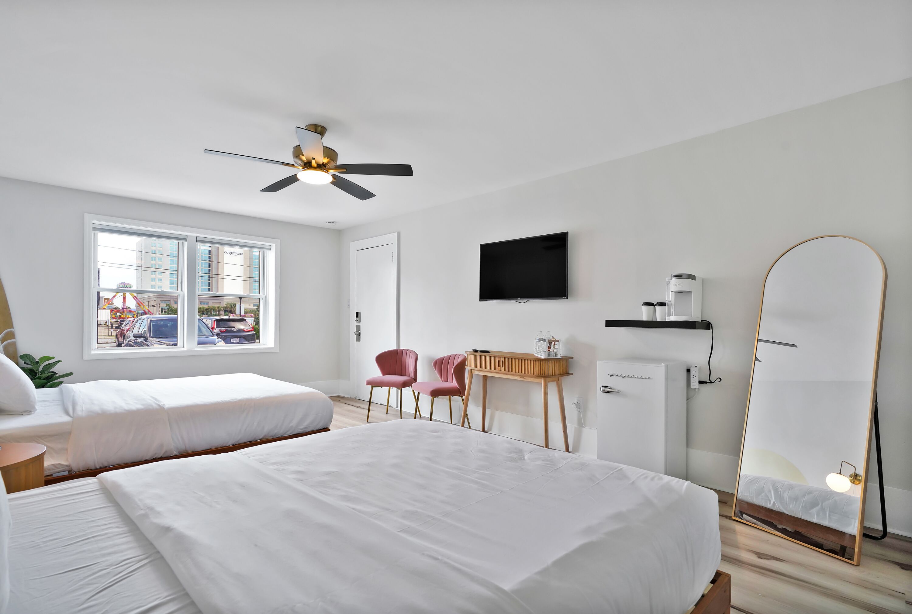 Een hotelkamer met twee bedden, een plafondventilator, een televisie, een spiegel en een bureau met stoel.