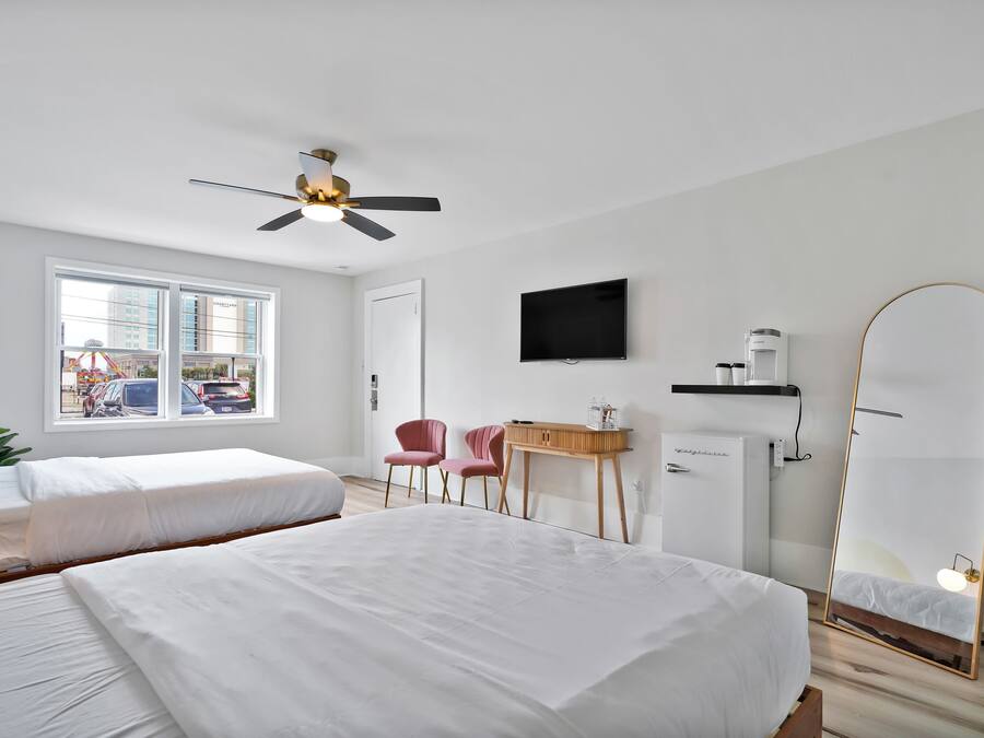 Een hotelkamer met twee bedden, een plafondventilator, een televisie, een spiegel en een bureau met stoel.