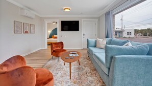 A modern living room with a sofa, armchairs, a coffee table, and a TV. - The Starlite Inn (Carolina Beach)
