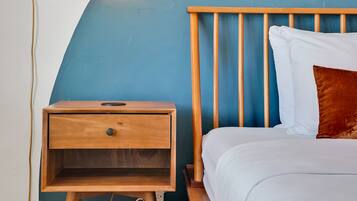 Une chambre avec une table de chevet en bois, un lit avec une literie blanche, un mur d’accent bleu et un luminaire suspendu.