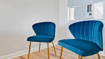 Twee blauwe fluweelstoelen met gouden poten in een kamer met houten vloer en een witte muur.