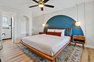 Un dormitorio con cama, ventilador de techo, mesitas de noche y alfombra.