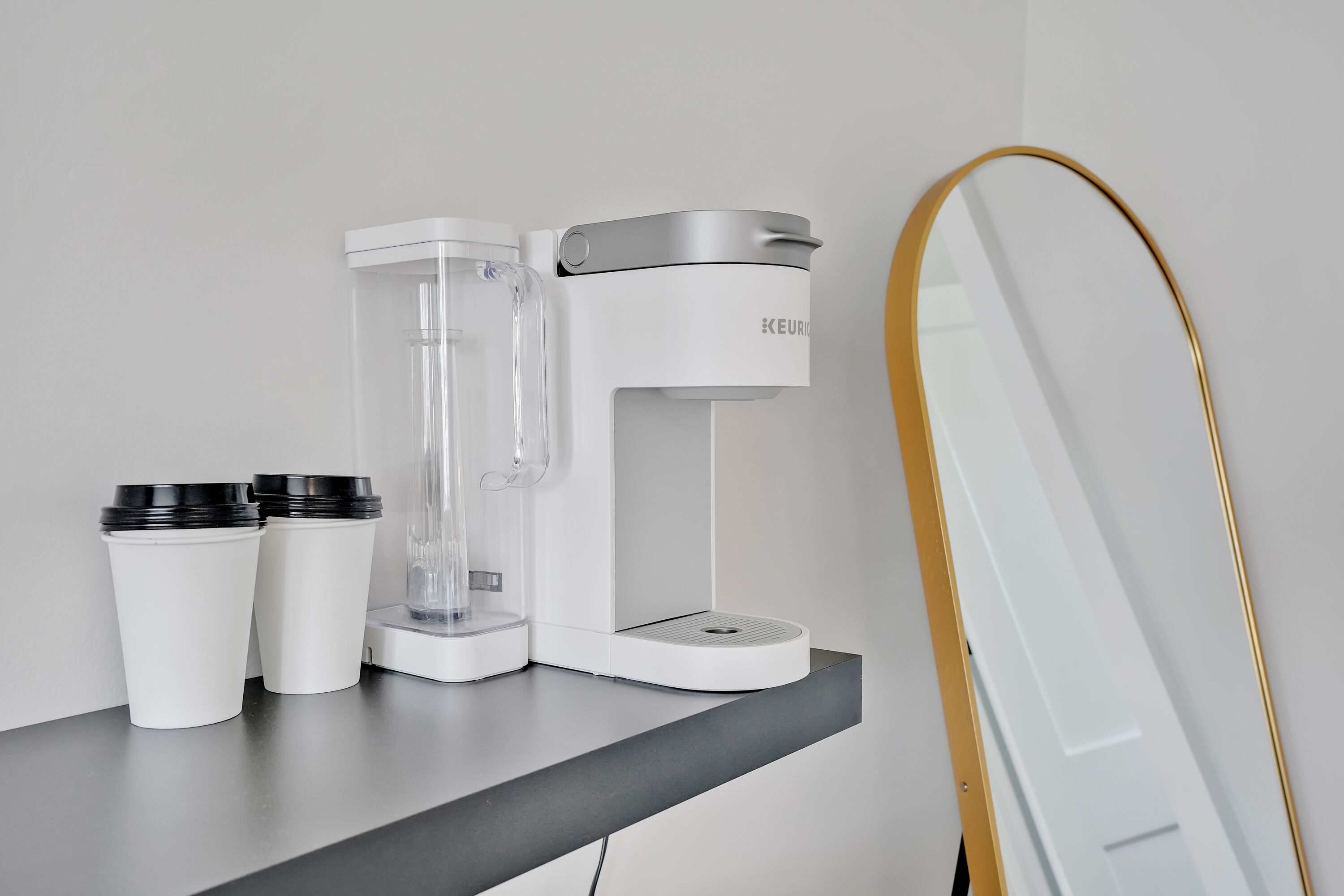 A coffee machine on a countertop with two disposable cups and a mirror.