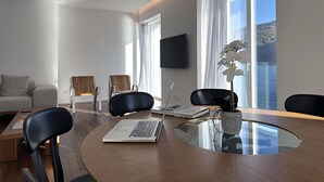 Un salon moderne avec une table à manger à plateau en verre, deux chaises noires, un canapé et un téléviseur à écran plat fixé au mur.