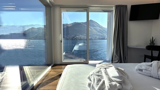 Une chambre d’hôtel dotée d’une grande fenêtre donnant sur un lac et des montagnes.