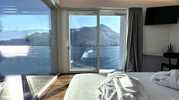 A hotel room with a large window offering a view of a lake and mountains.