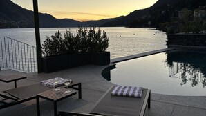 Un espace aménagé au bord de la piscine, avec des chaises longues, une table sur laquelle se trouve un verre de vin et une lampe.