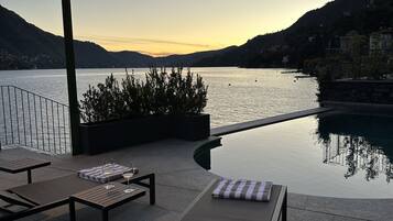 A poolside area with lounge chairs, a table with a glass of wine, and a lamp.