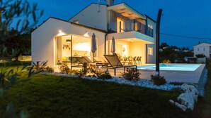 Una casa moderna de dos pisos con piscina, mobiliario exterior y un jardín cuidado.