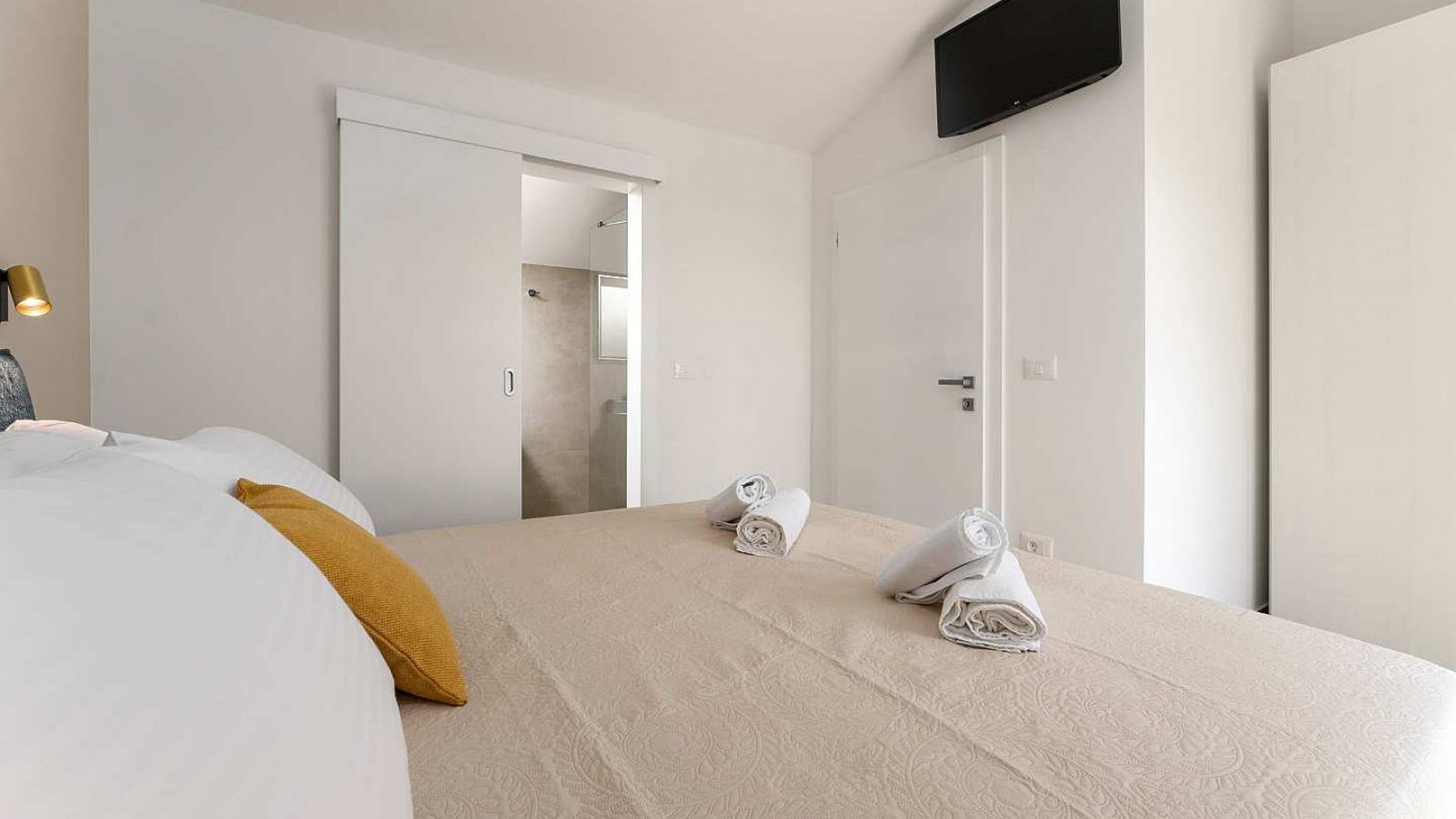 Ein Hotelzimmer mit einem Bett, einem an der Wand montierten Fernseher und einem durch eine offene Tür einsehbaren Badezimmer.