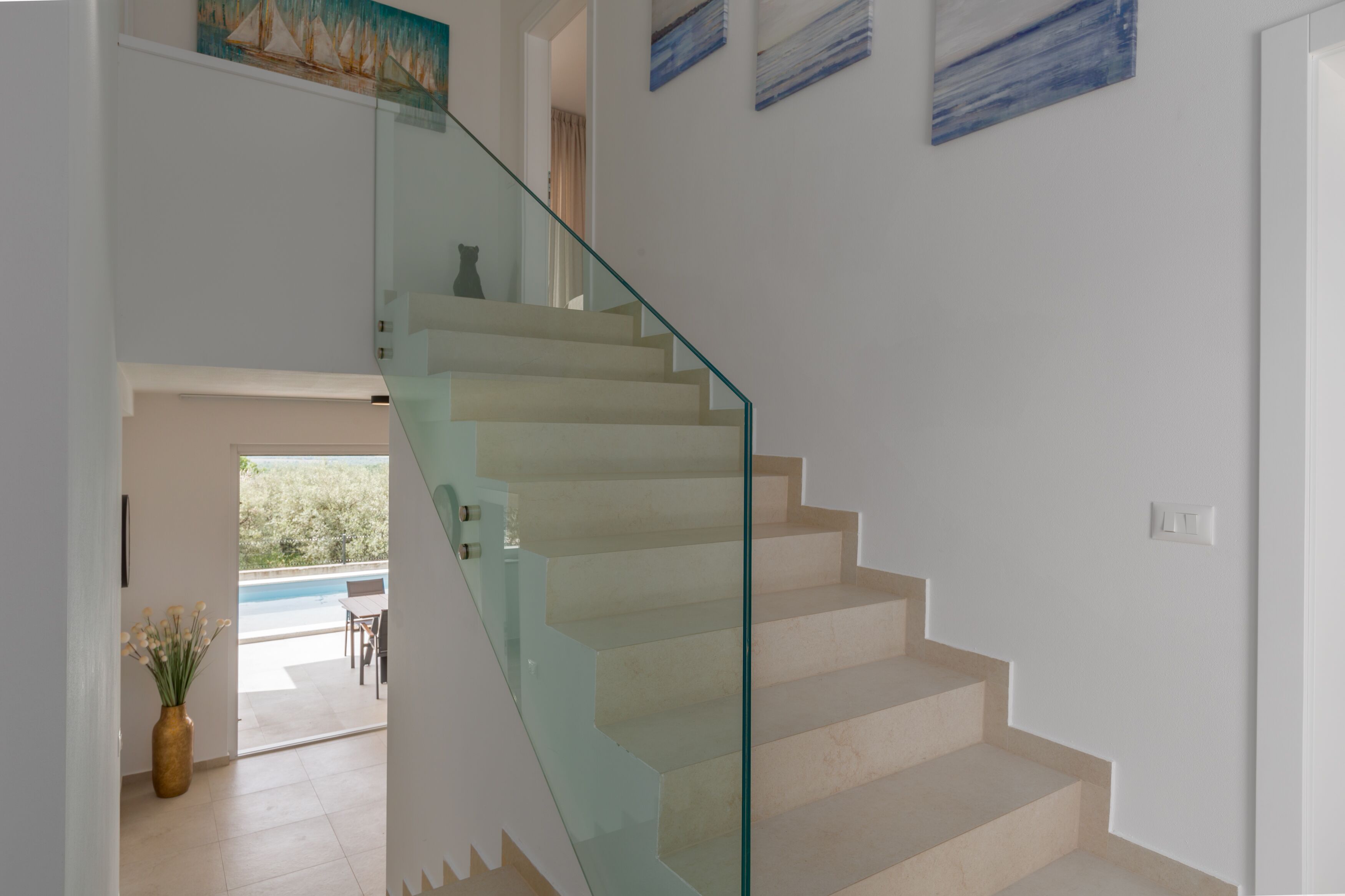 A modern staircase with glass railings leading to a room with a view of a swimming pool.