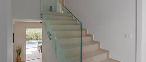 A modern staircase with glass railings leading to a room with a view of a swimming pool.