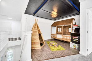 Une salle de jeux pour enfants avec une mezzanine, une maisonnette et une zone dédiée aux jeux d’arcade.