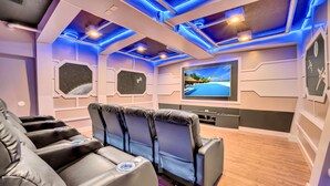 Ein Heimkino mit Liegesesseln, einem großen Flachbildfernseher und einem Wanddesign mit Sternenmotiv.