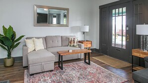 Una sala de estar con sofá, una mesa de centro, una lámpara, un espejo y un gran ventanal.
