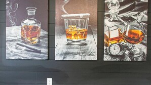 Zona de bar con tres cuadros que muestran botellas y vasos de whisky.