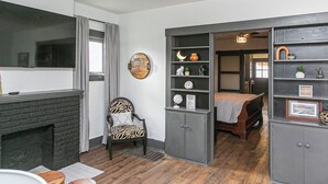 Una habitación con chimenea, un sillón estampado con diseño de cebra, una cama y una estantería con diversos objetos.