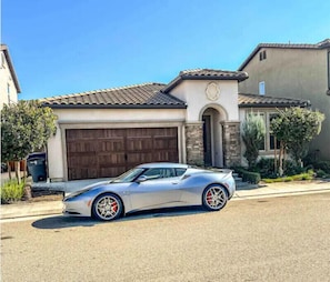 Une maison moderne avec un garage, une allée et une voiture de sport argentée garée devant.