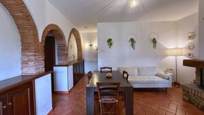 A dining area with a long table, chairs, and a white sofa. There are brick arches and a stone fireplace.